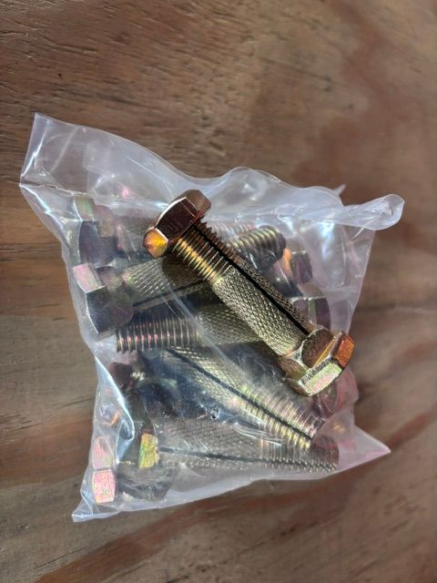 Clear plastic bag of metal bolts and nuts on a wooden surface