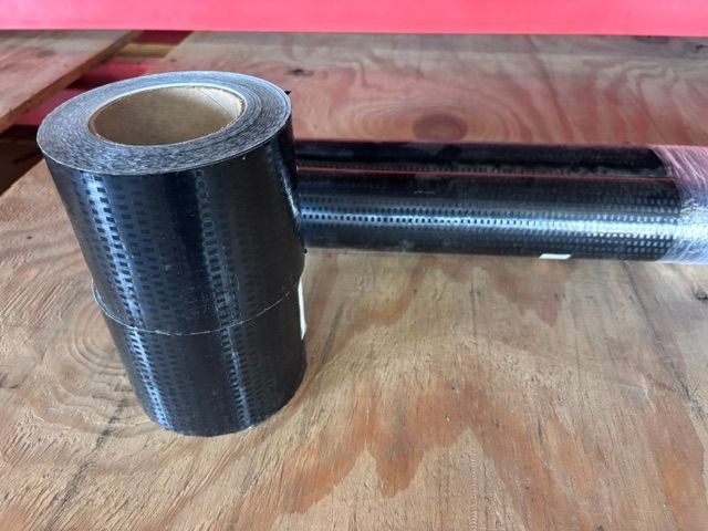 Two rolls of black plastic wrap on a wooden surface