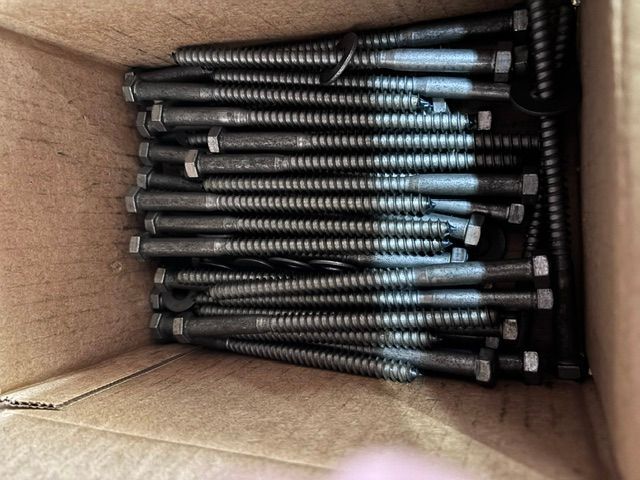 Open cardboard box filled with stacked dark metal screws or bolts