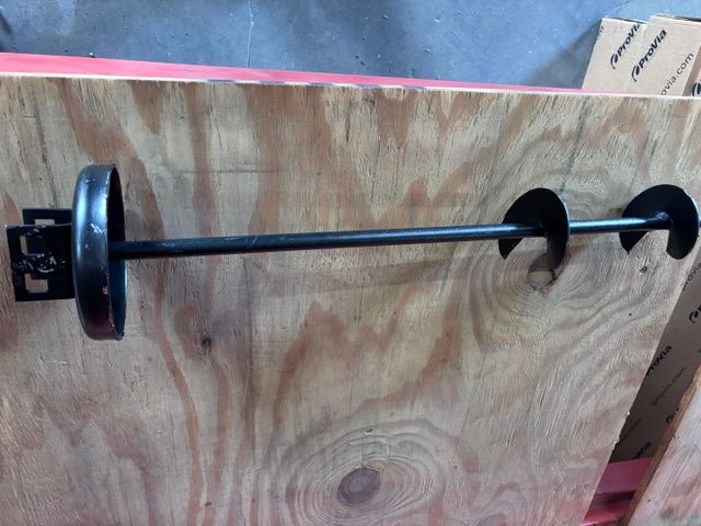 Black rod with two circular discs mounted on a plywood board in a workshop setting