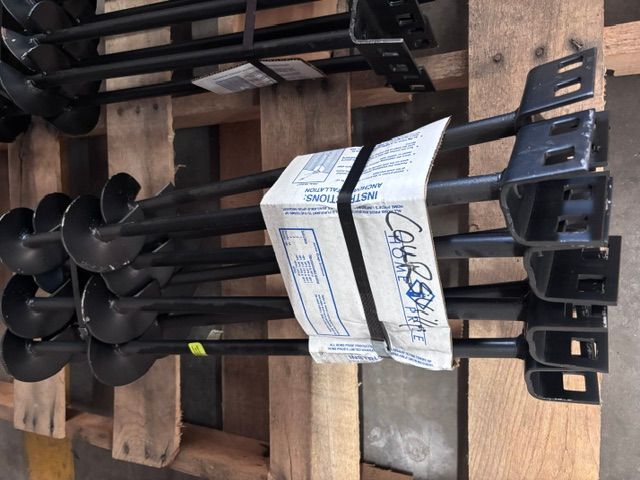 Bundle of black metal tools or stakes tied with a label, stacked on wooden pallets in a warehouse.