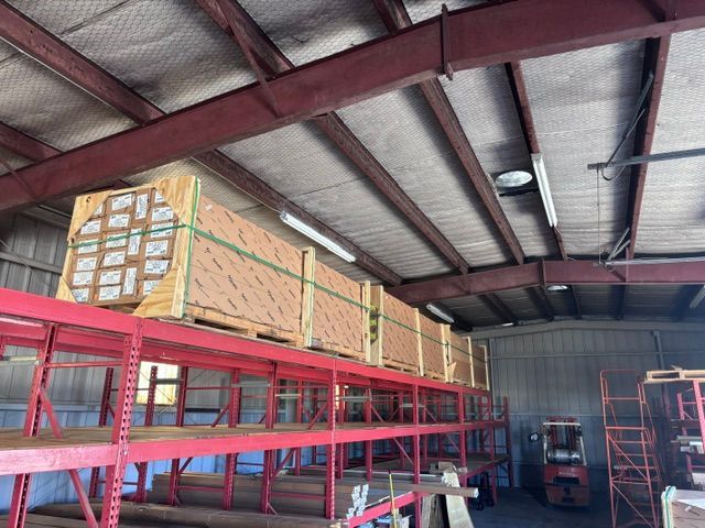 Large wrapped pallets stacked on a red warehouse mezzanine under a metal roof