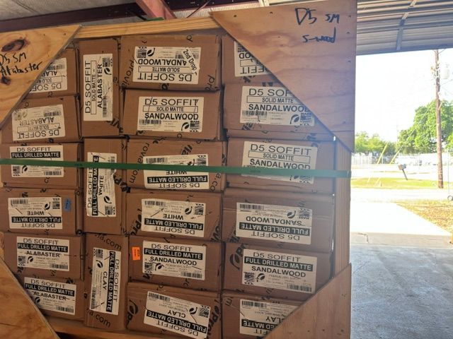 Stacked drywall boxes on a pallet in a warehouse loading area near an open bay door.