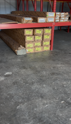 Pallets of lumber and stacked boxes stored on metal warehouse shelving.