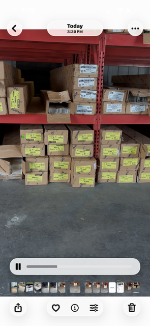 Stacks of cardboard boxes on warehouse shelves and the floor, many labeled and wrapped in a storage area.