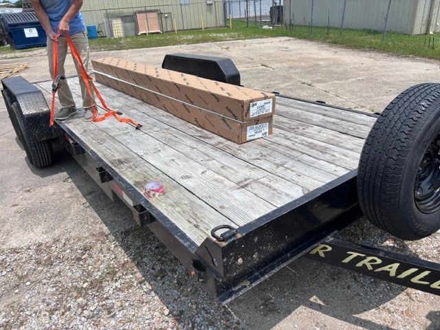 Flatbed trailer with large wooden beam secured by orange straps in an outdoor lot