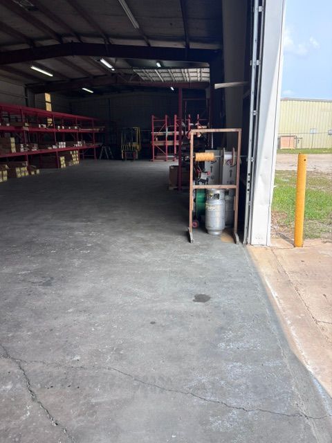 Empty warehouse interior with metal shelving, open roll-up door, and concrete floor.