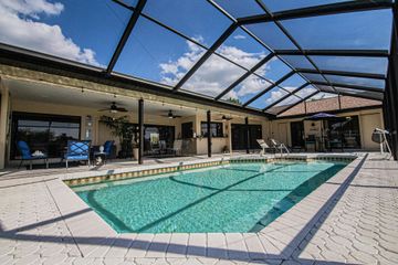 A swimming pool set in a covered patio area with lounge furniture and a screen enclosure under a blue sky.