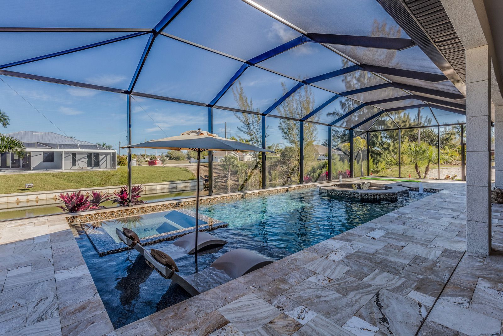 A screened-in patio featuring a swimming pool with submerged lounge chairs, a patio umbrella, and a stone deck.