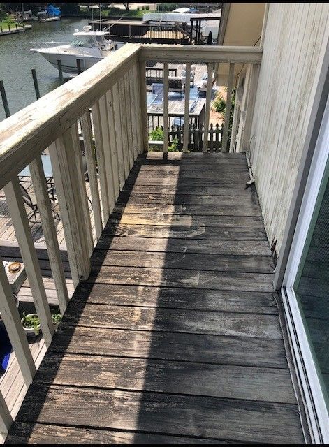 a wooden deck with a sliding glass door and a boat in the background . | Corpus Christi, TX | GT Roofing