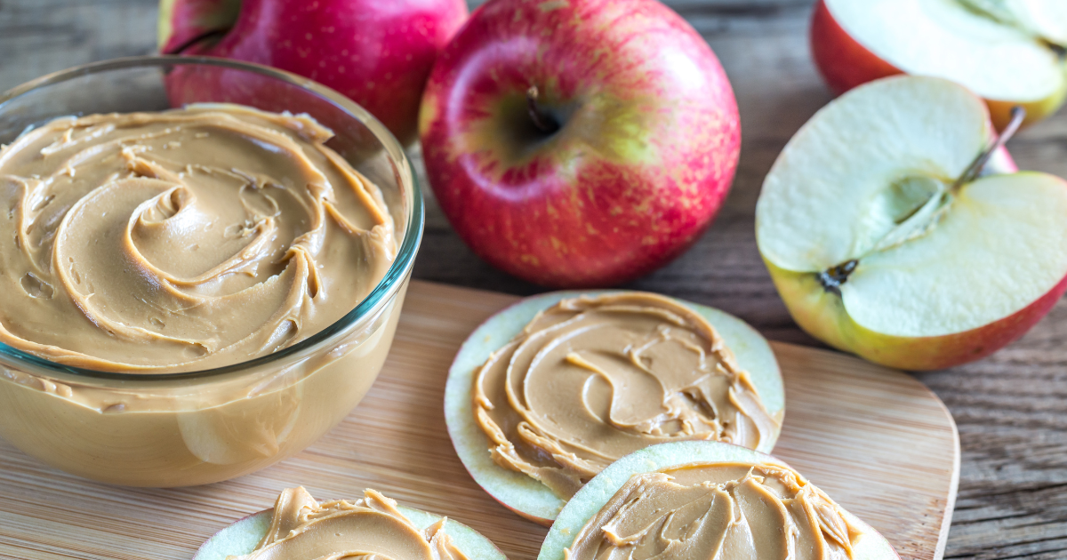 There is a bowl of peanut butter and apples on the table.