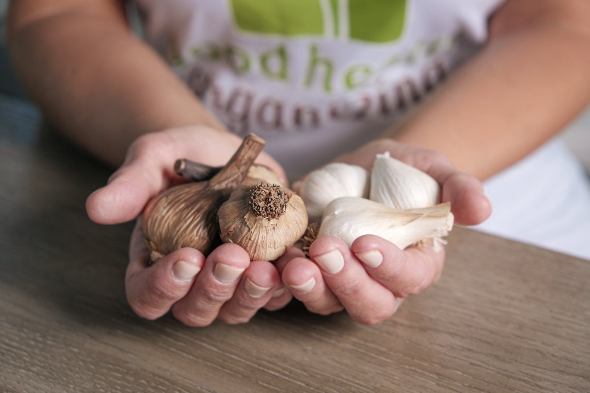 A person is holding three different types of garlic in their hands.