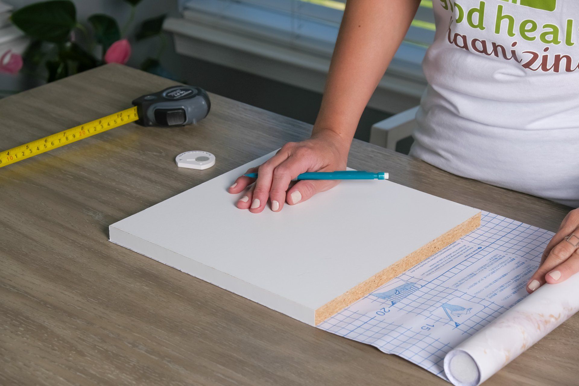 A woman is measuring a piece of paper with a tape measure.