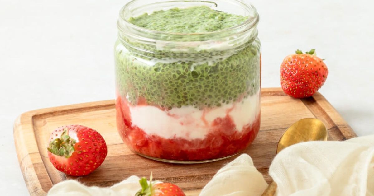 A jar of food with strawberries and yogurt on a wooden cutting board.