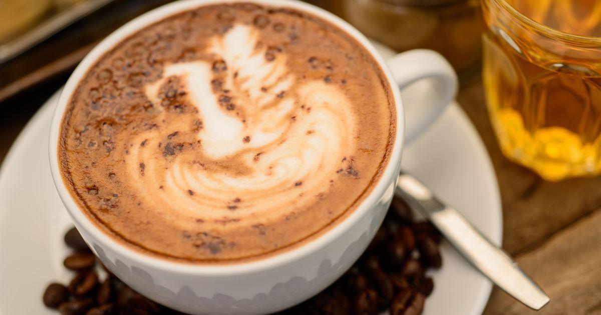 A cup of peppermint moca is sitting on a plate next to coffee beans and a glass of tea.
