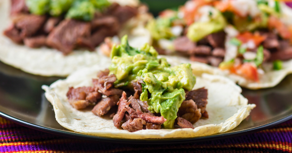 A close up of a taco with guacamole and meat on a plate.
