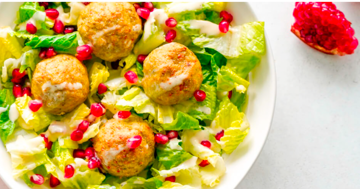 A salad with meatballs , lettuce , and pomegranate seeds on a plate.