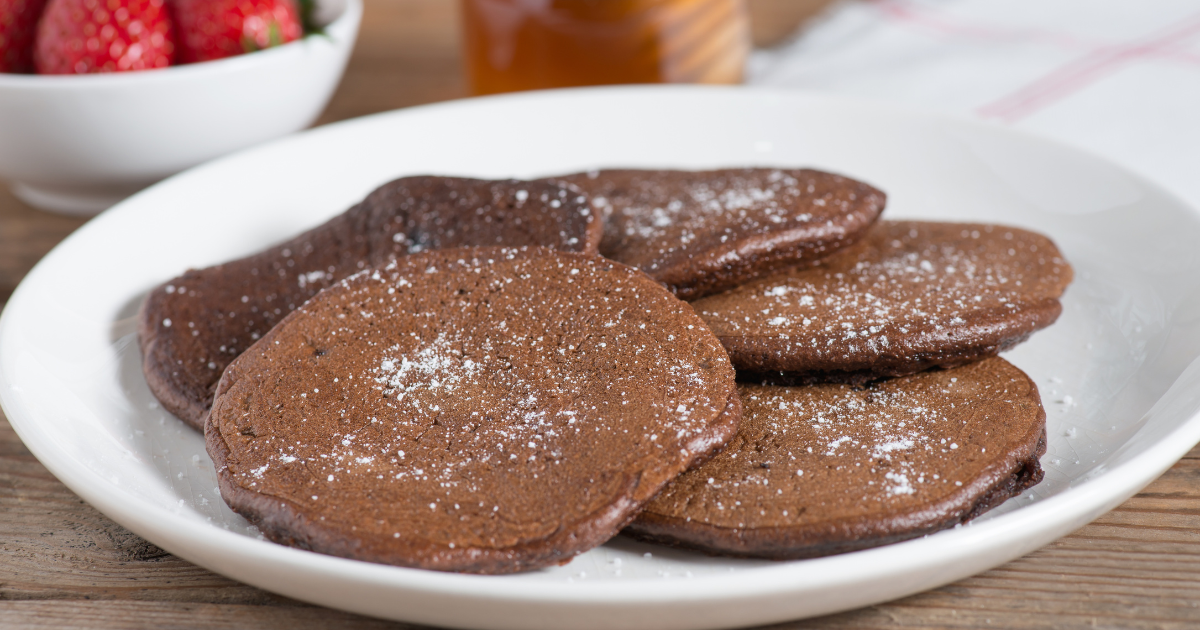 A white plate topped with chocolate pancakes next to a bowl of strawberries.
