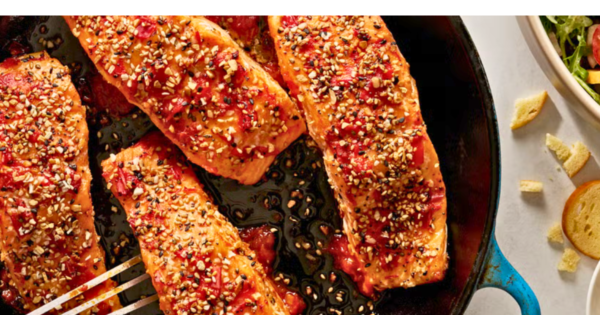 A skillet filled with salmon and a fork on a table.