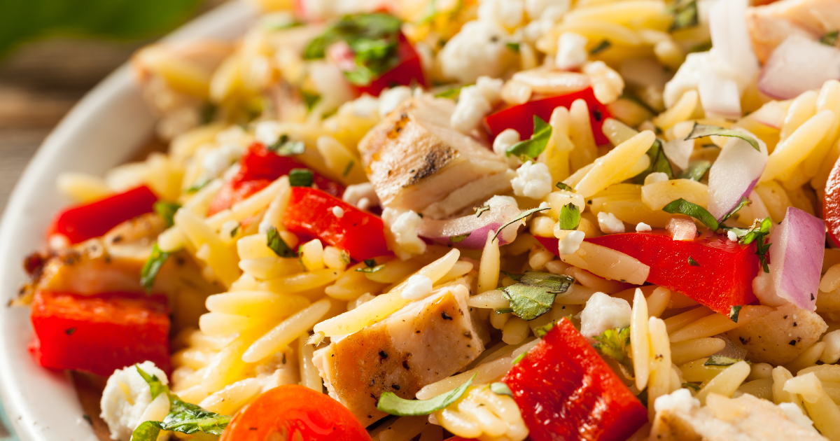 A close up of chicken and orzo with tomatoes , onions and feta cheese.