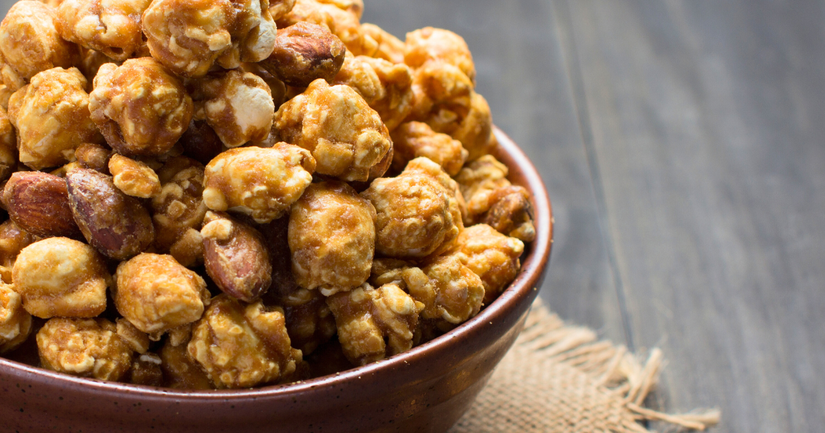 A bowl of chocolate popcorn and peanuts on a wooden table.