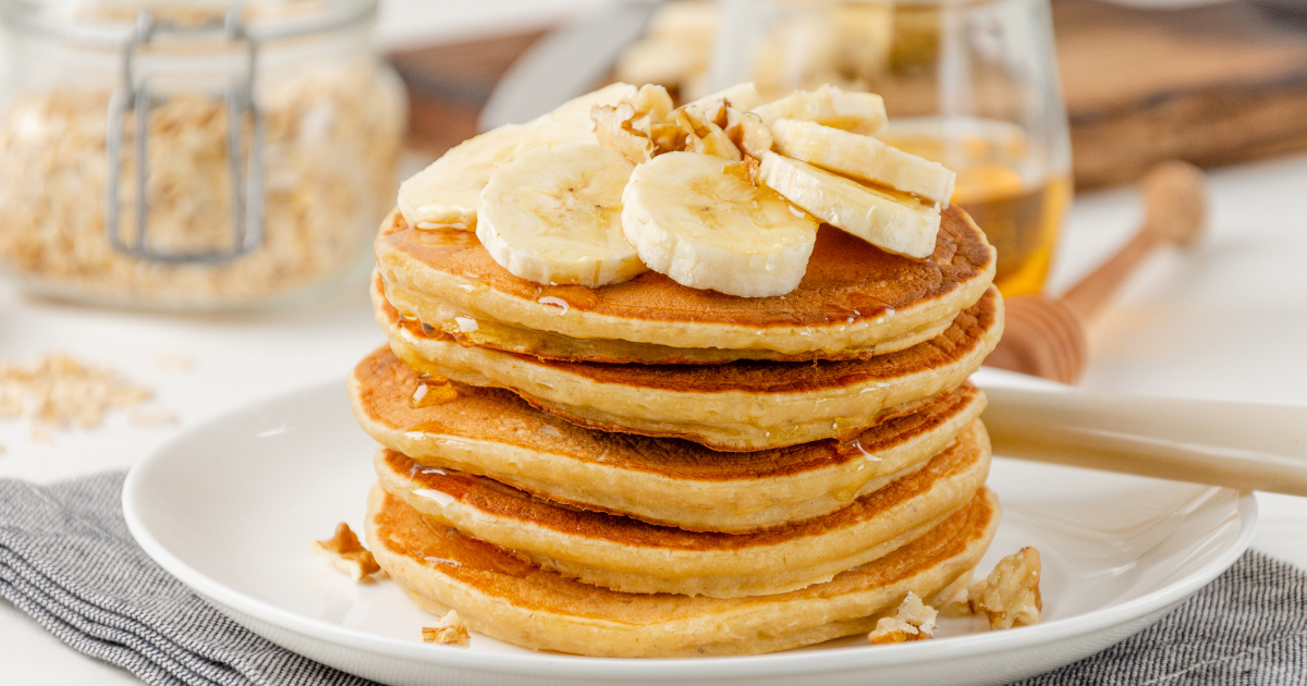 A stack of pancakes with bananas on top on a white plate.