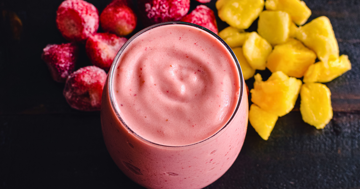 A smoothie in a glass next to strawberries and pineapple slices.