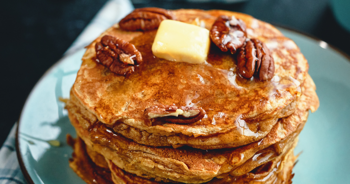 A stack of sweet potato pancakes with pecans and butter on a blue plate.