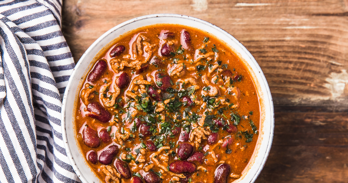 A bowl of chili with beans and rice on a wooden table.
