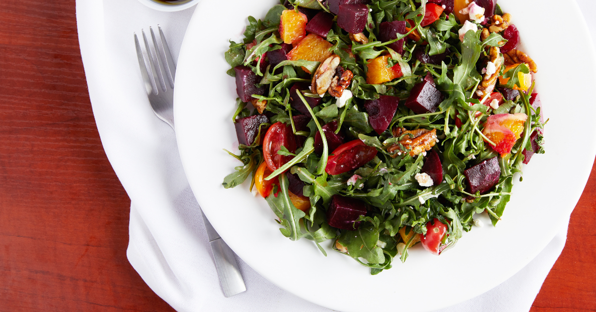 A white plate topped with a salad and a fork on a wooden table.