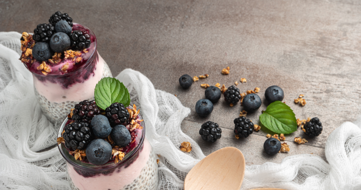 A close up of two desserts with blueberries and blackberries on a table.