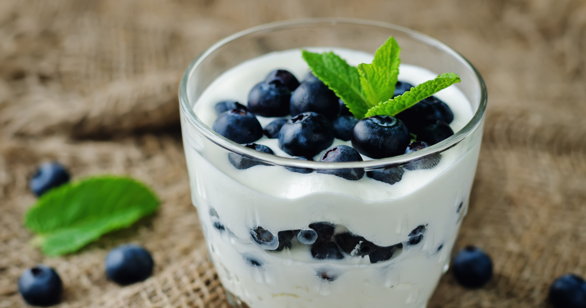 A glass of yogurt with blueberries and mint leaves on top.