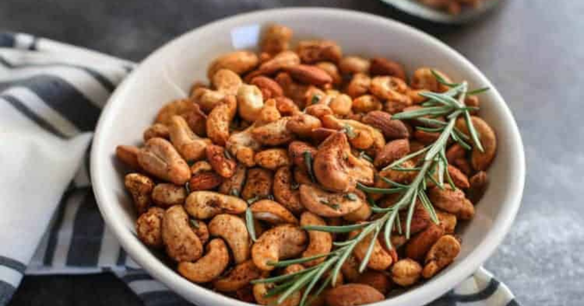 A white bowl filled with nuts and rosemary on a table.