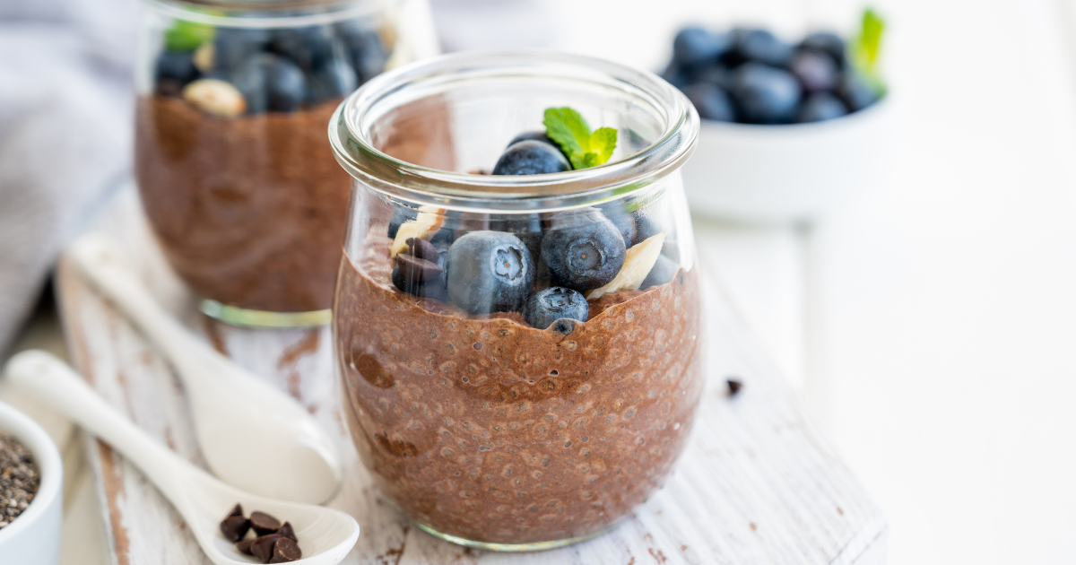 A jar of chocolate chia pudding with blueberries and almonds on a table.