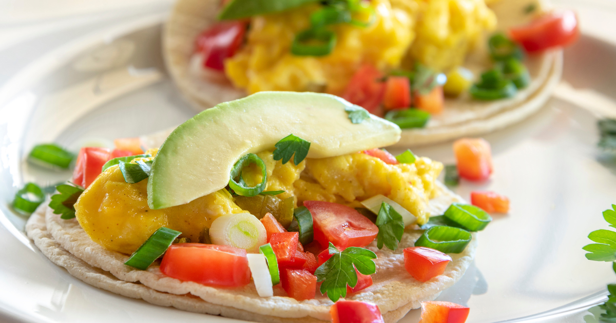 A close up of a plate of food with eggs , avocado , tomatoes and onions.