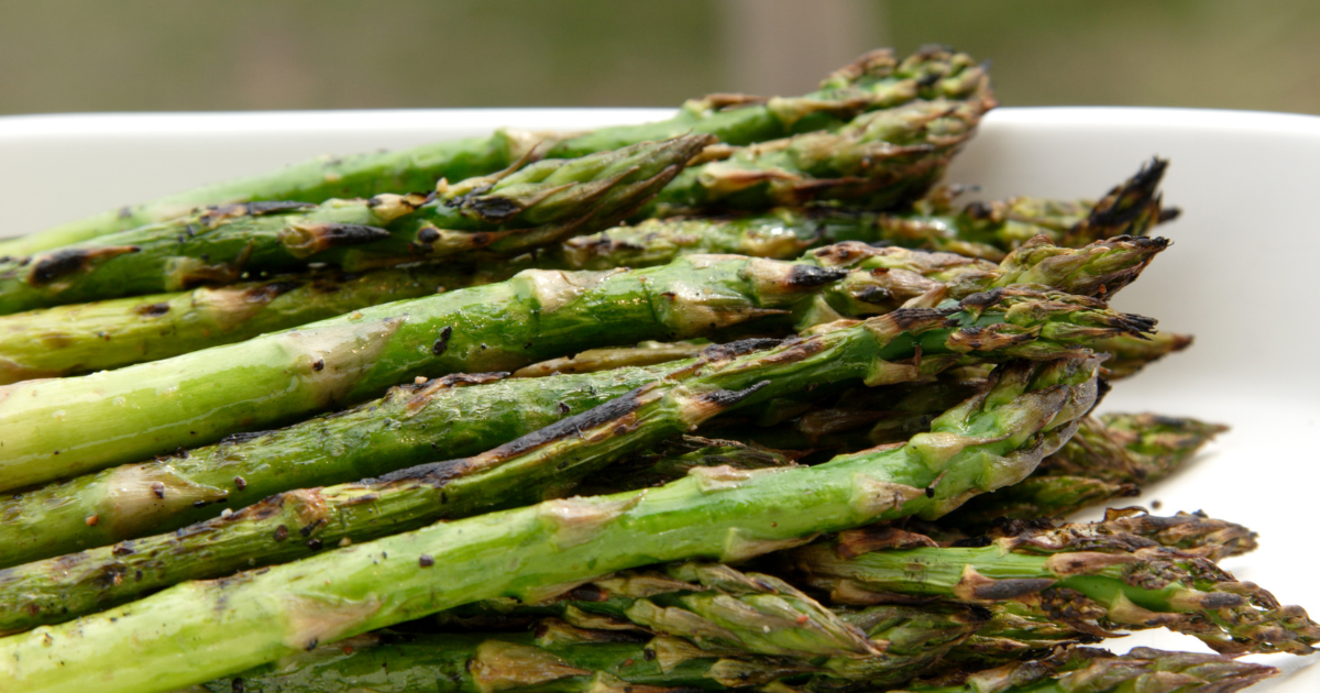 A white plate topped with grilled asparagus on a table.