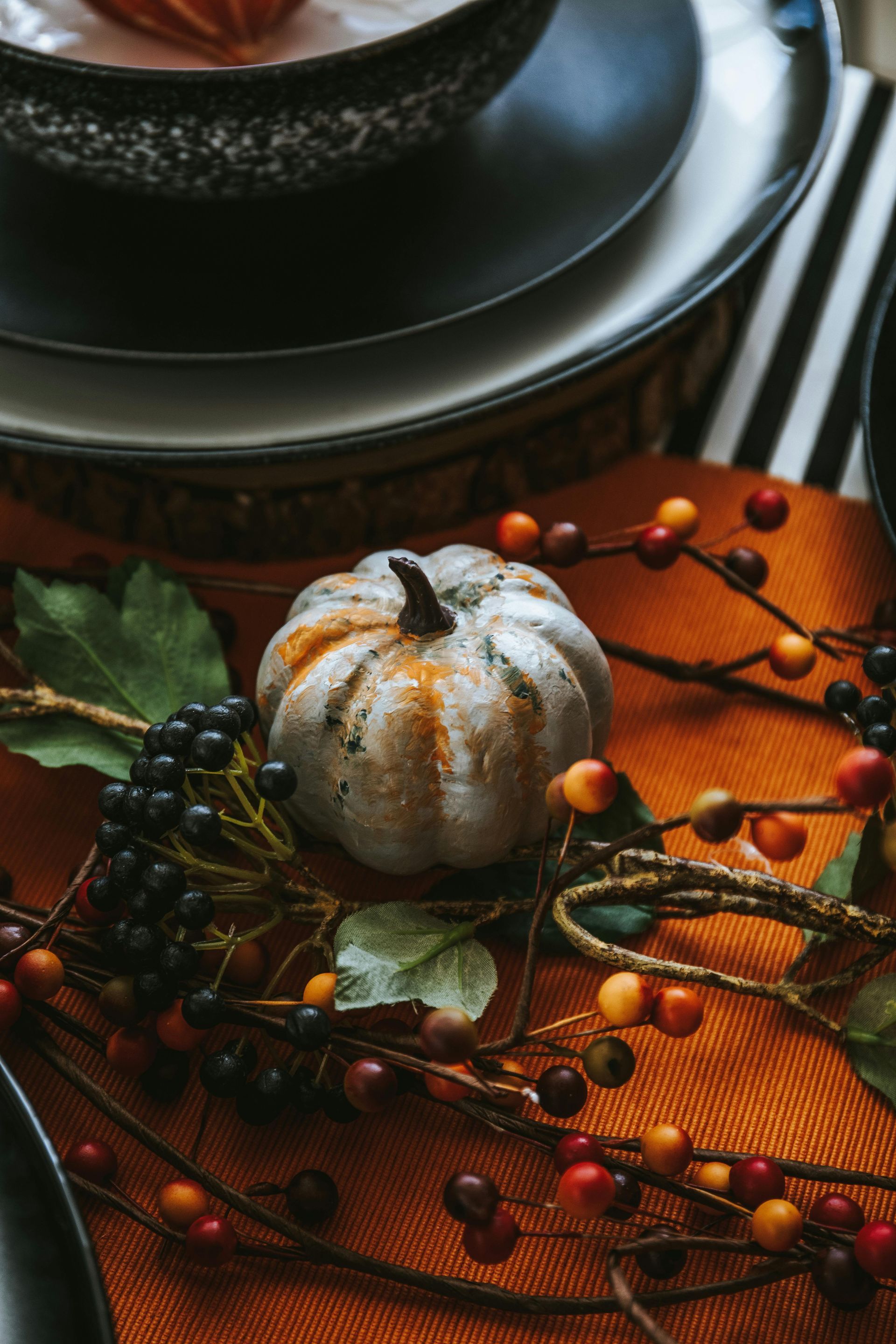 A small pumpkin is sitting on top of a table next to plates and berries.