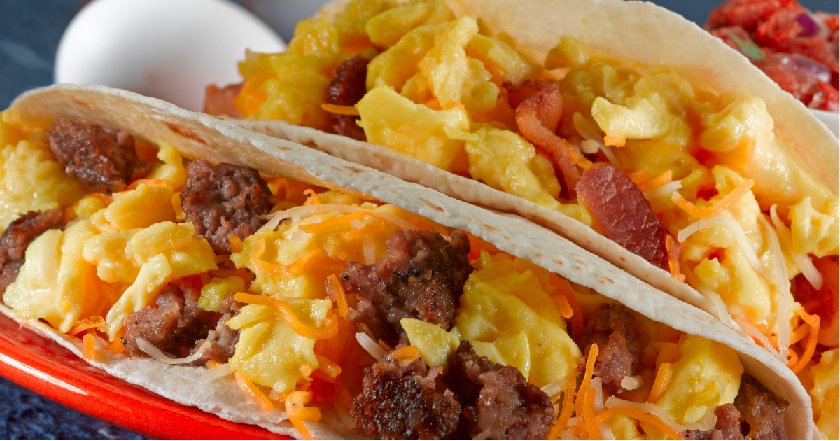 A close up of two breakfast tacos on a red plate.