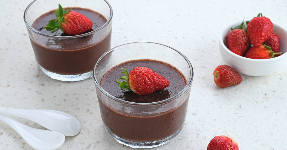 Two glasses of chocolate pudding with strawberries on top.