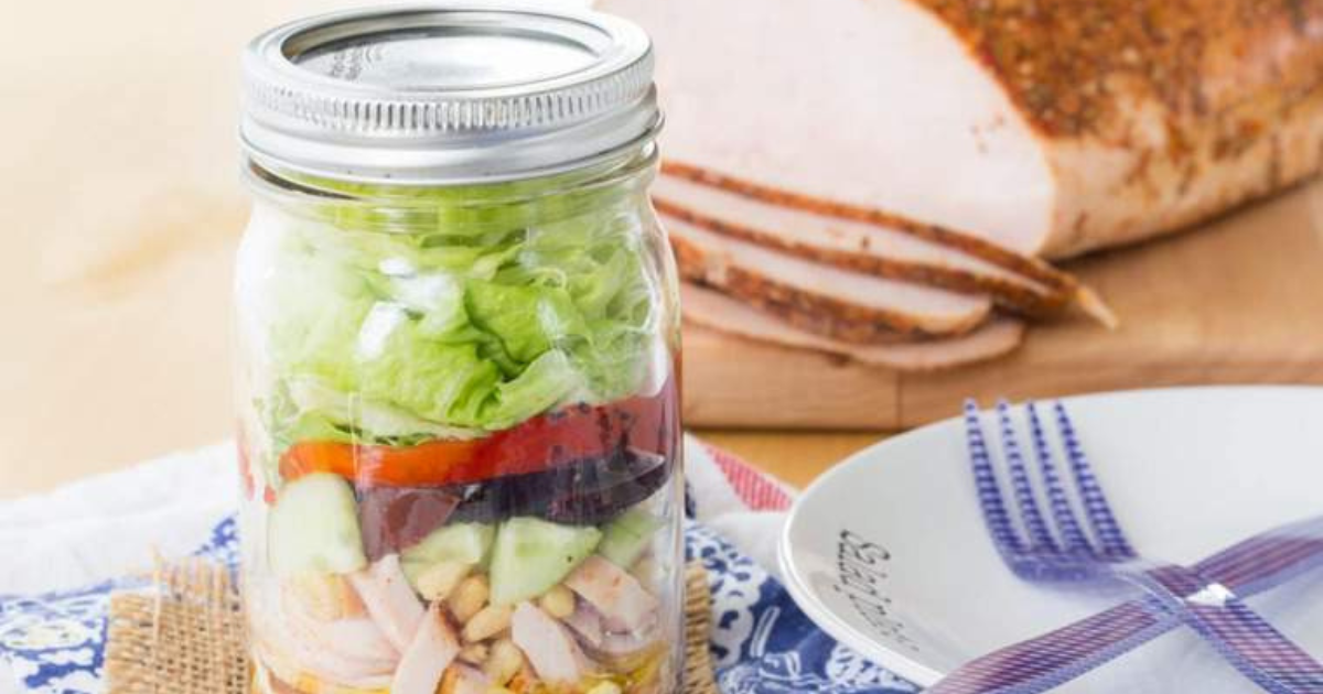 A salad in a mason jar is sitting on a table next to a plate and fork.