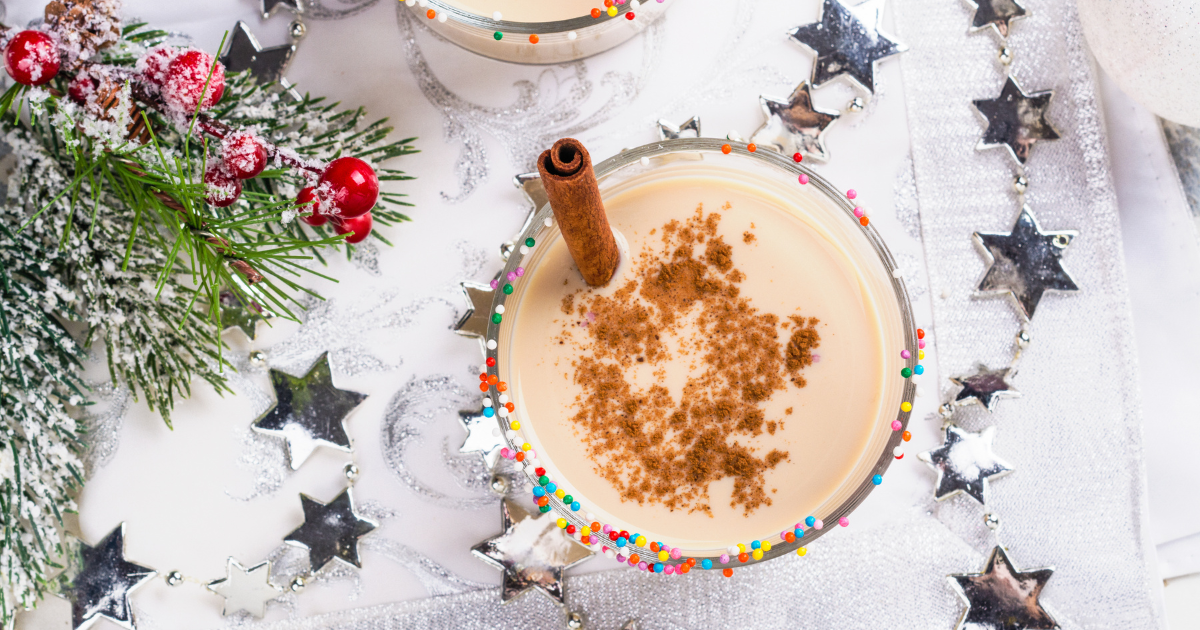 Two glasses of vegan eggnog with cinnamon and sprinkles on a table.