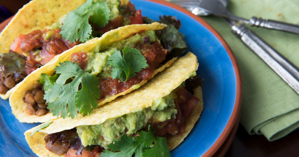 A blue plate topped with three tacos with guacamole and salsa.