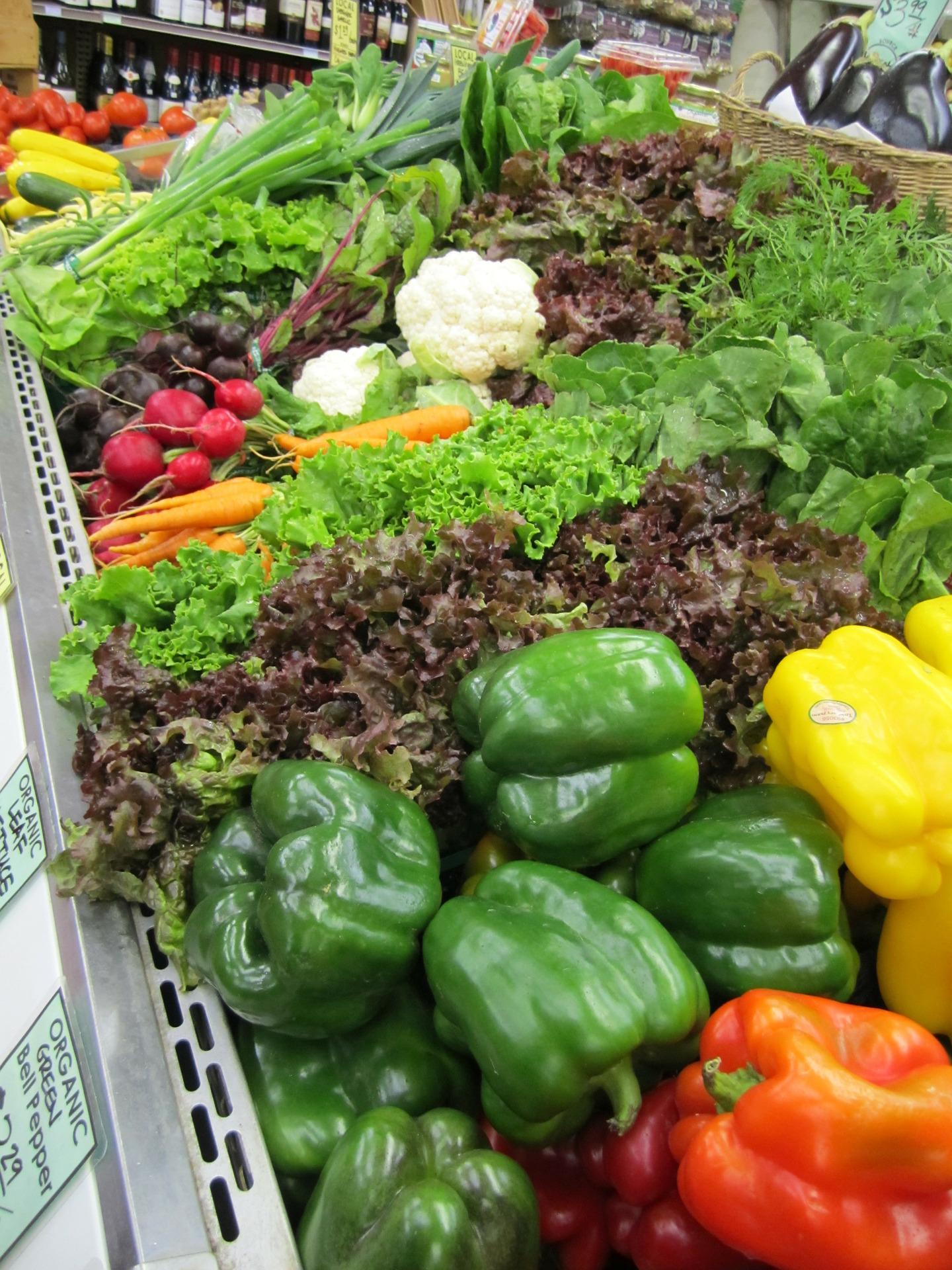 A variety of vegetables are displayed on a shelf in a grocery store.