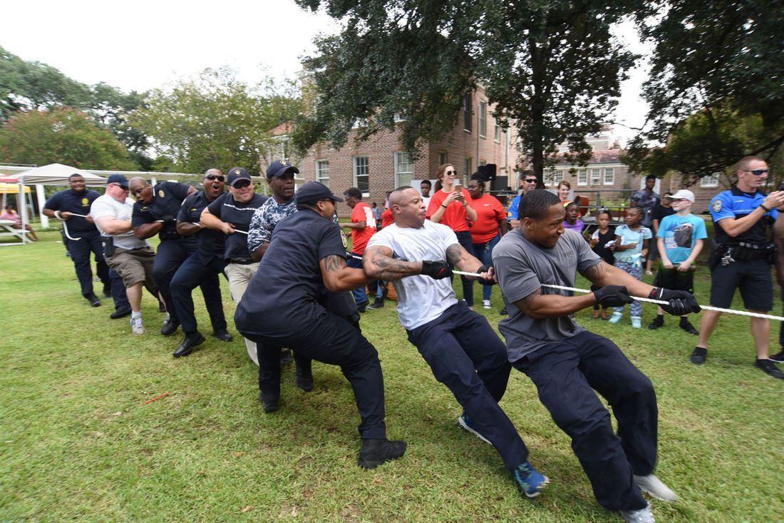 People engaged in a tug-of-war on a grassy field; other people watch in background.