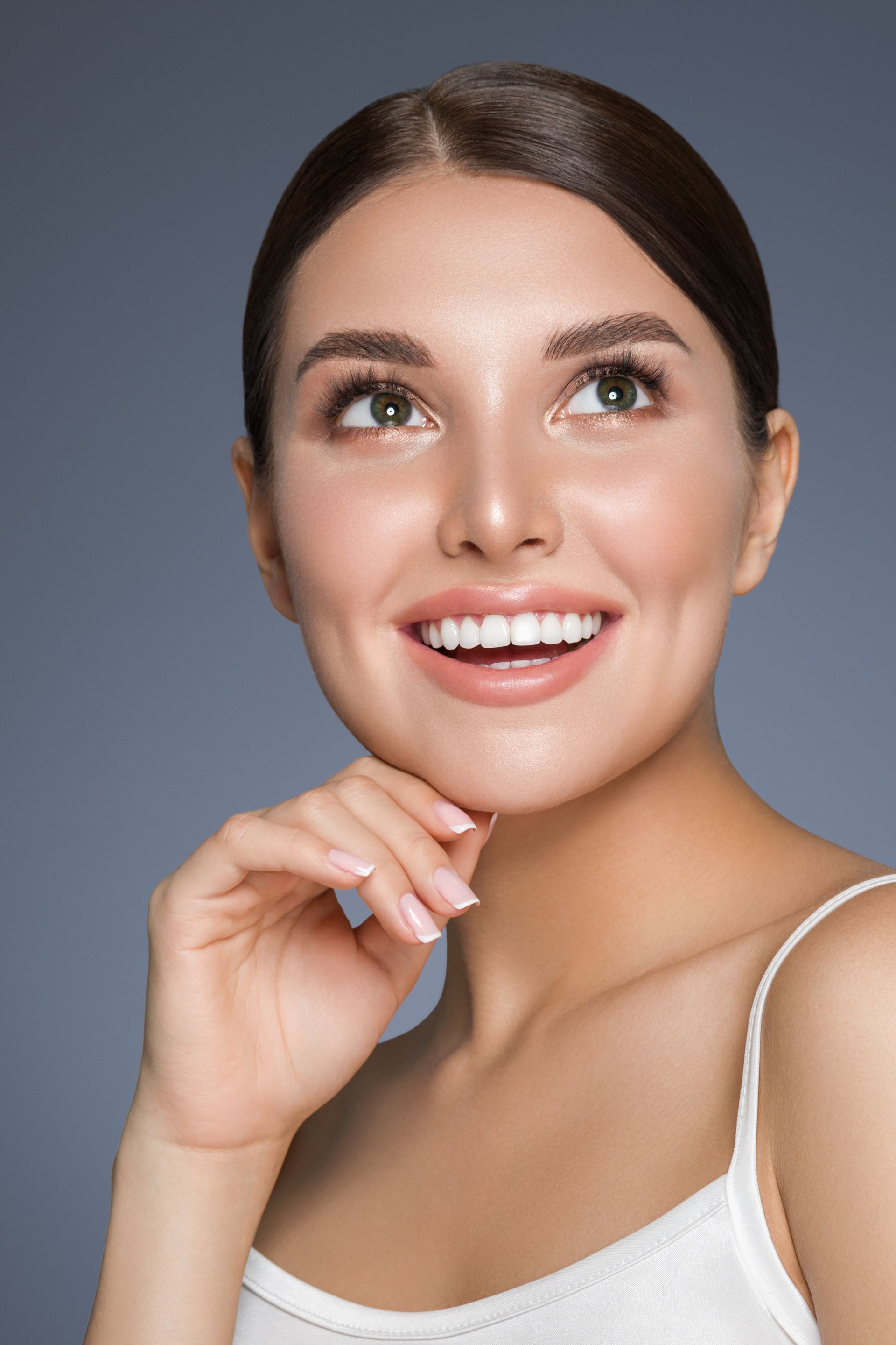 a woman in a white tank top smiles with her hand on her chin
