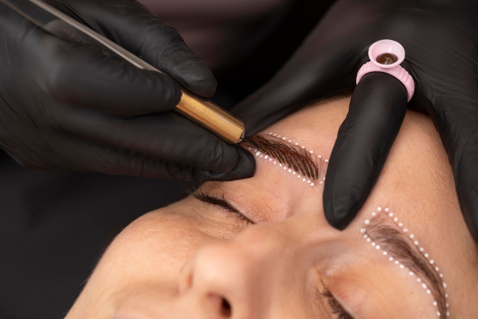a woman is getting her eyebrows done by a person wearing black gloves