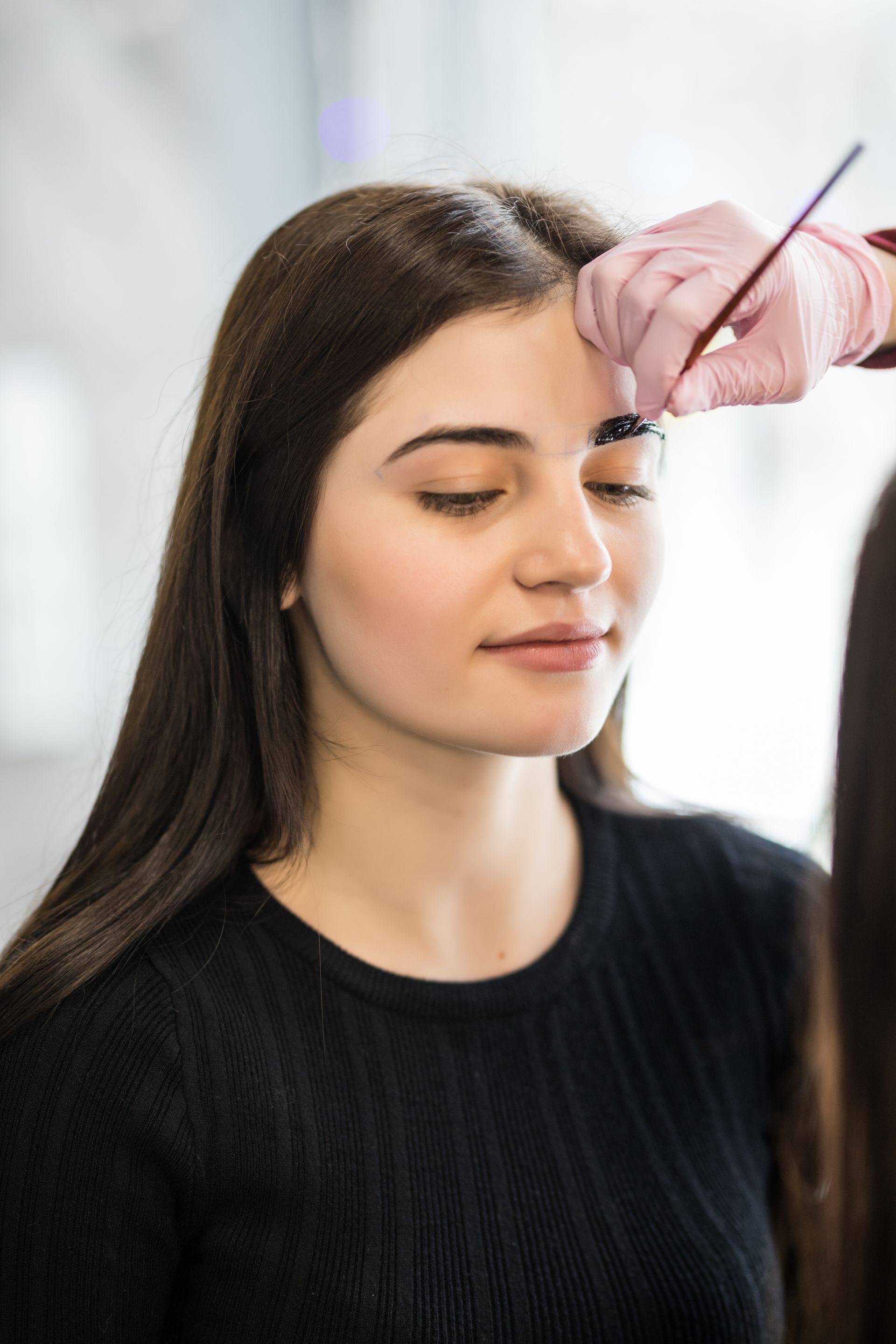 a woman is getting her eyebrows painted by a person wearing pink gloves