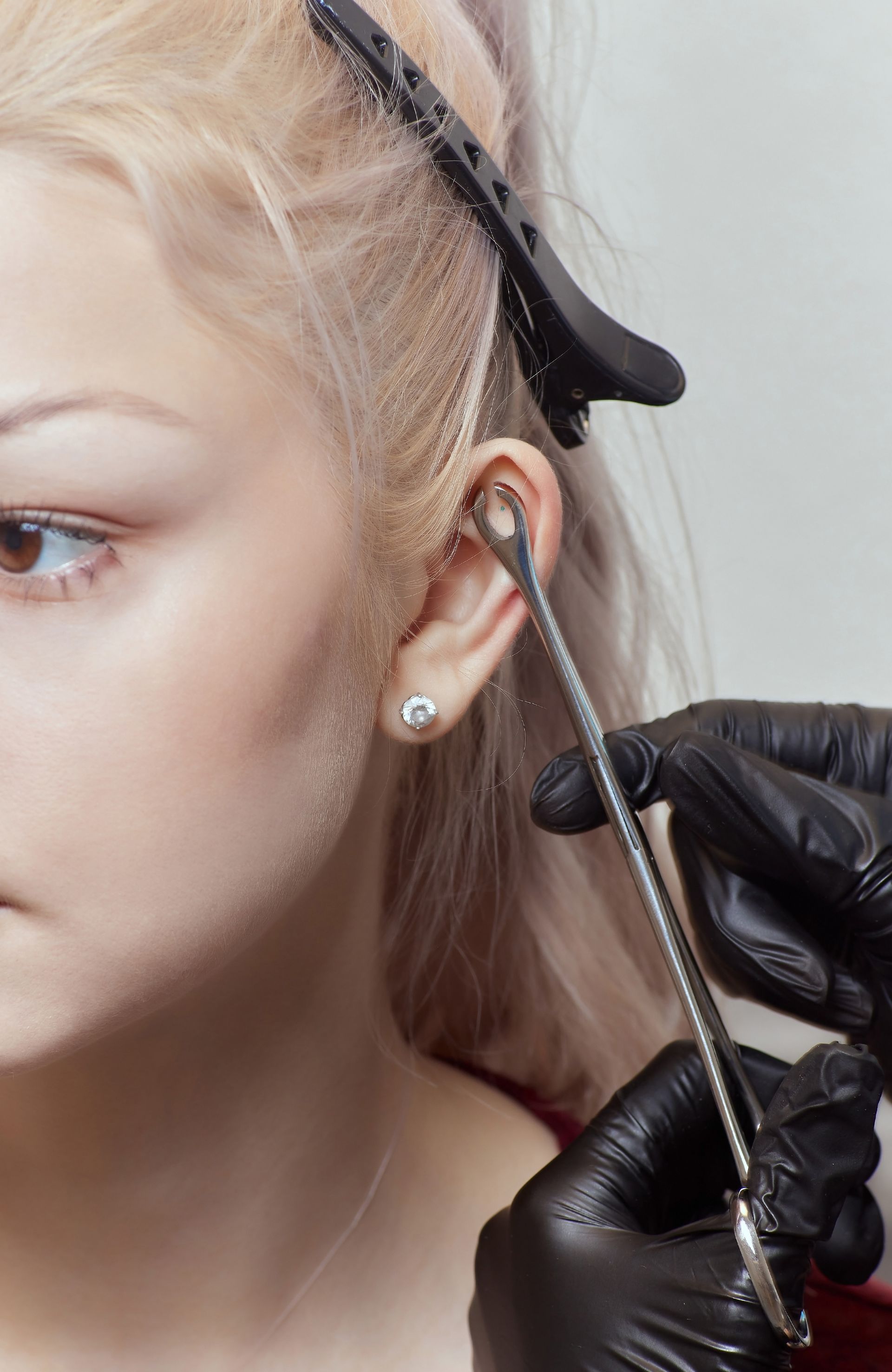 a woman is getting her ear pierced by a person wearing black gloves