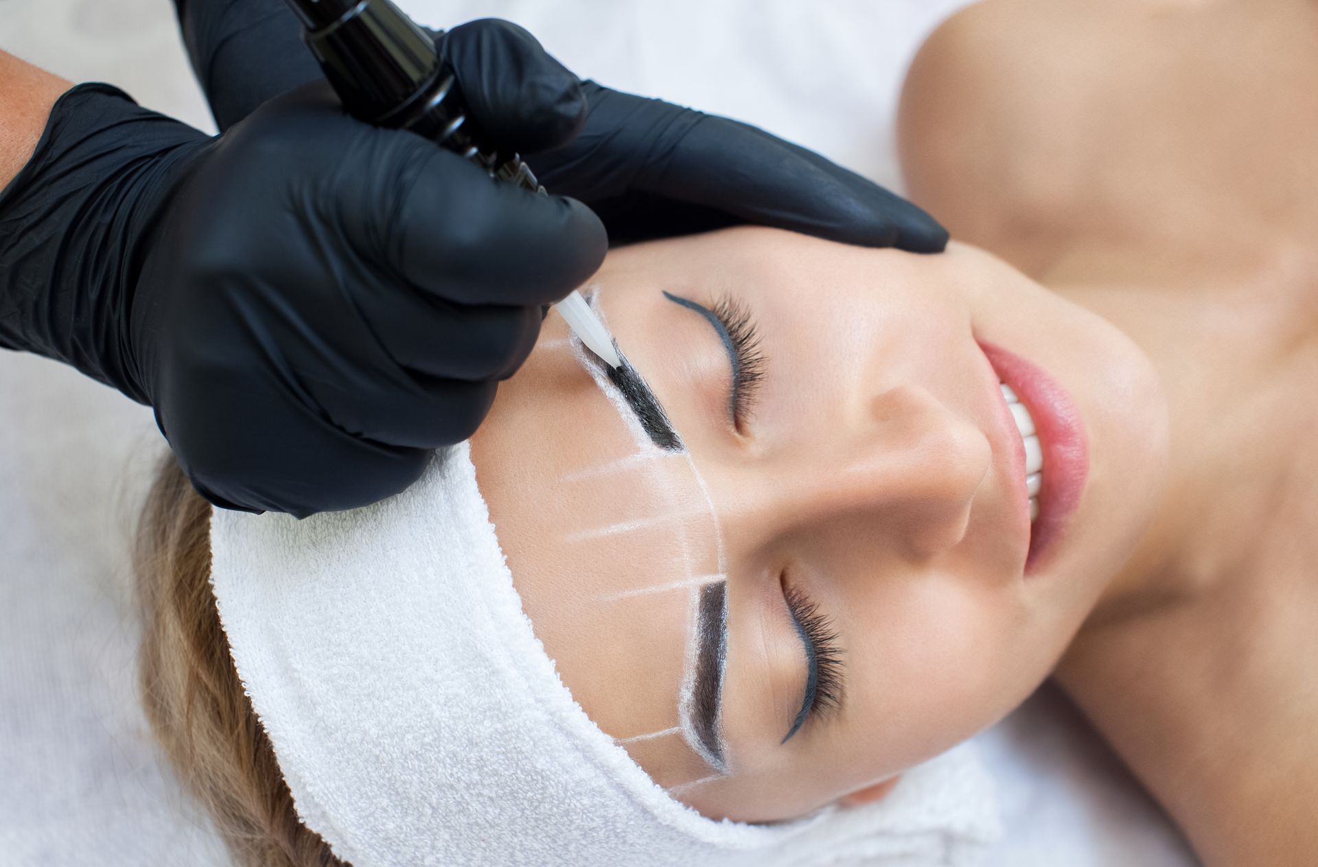 a woman is getting her eyebrows tattooed by a person wearing black gloves