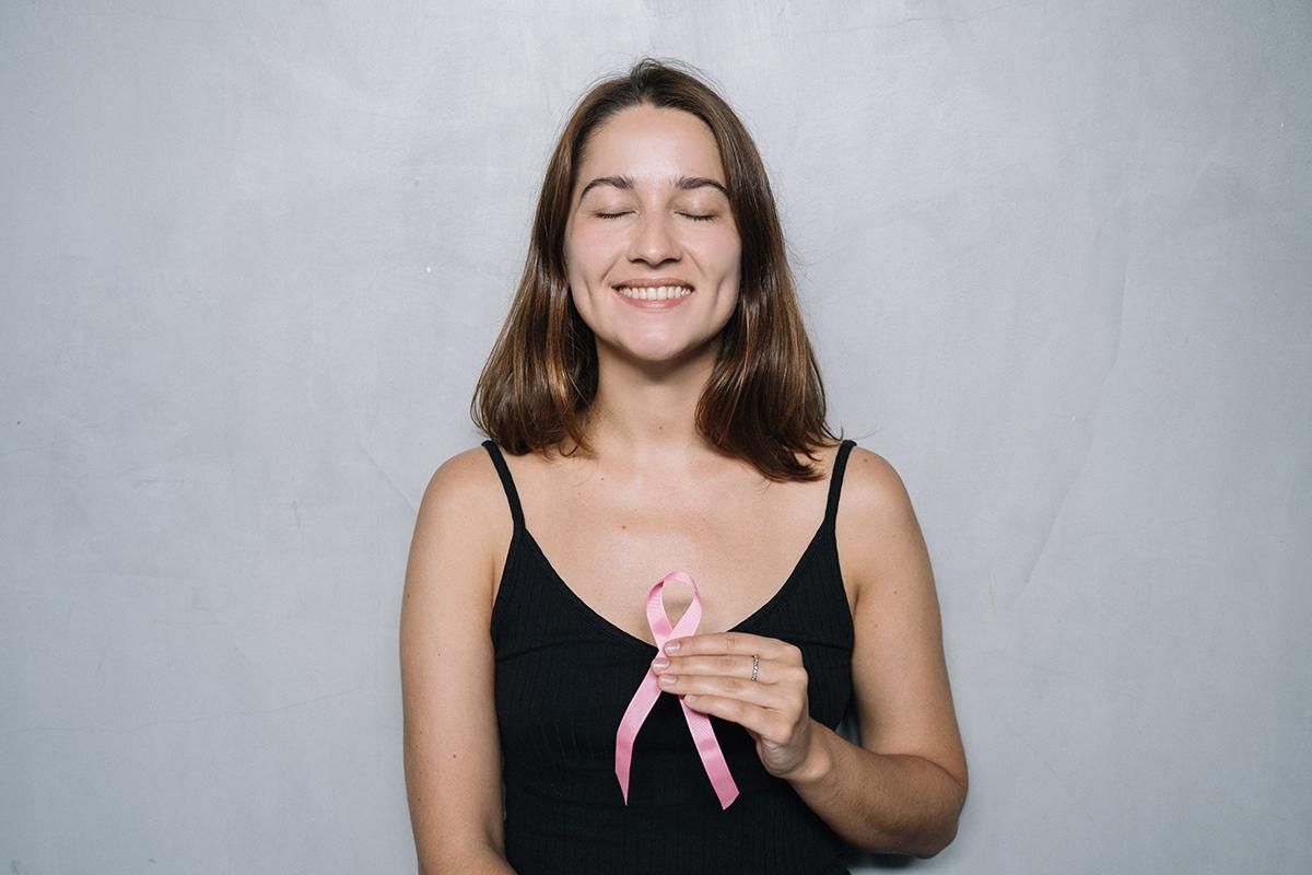 Smiling person holding a pink ribbon against a plain gray background